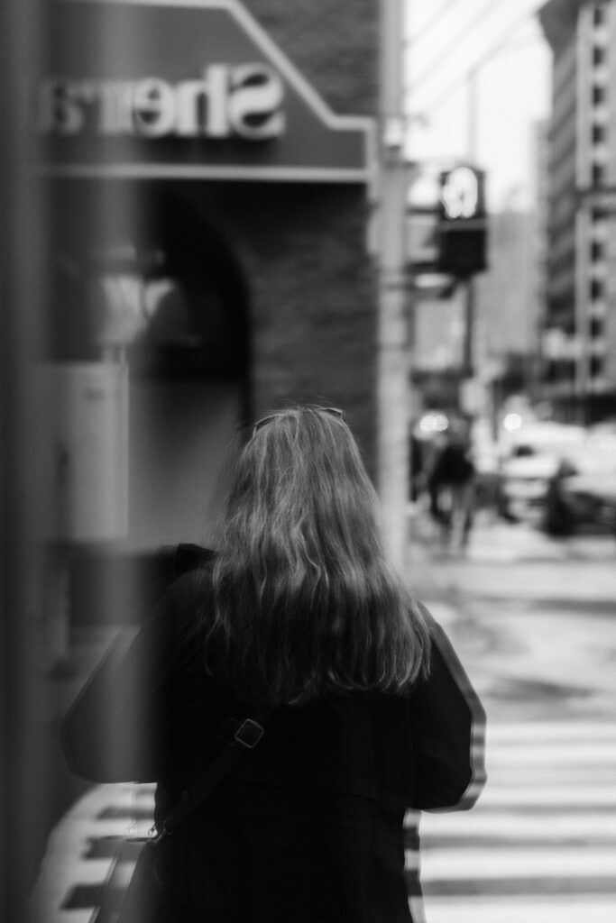 A woman waiting for the green light, beautifully reflected in the window, capturing a quiet, reflective moment in the city.