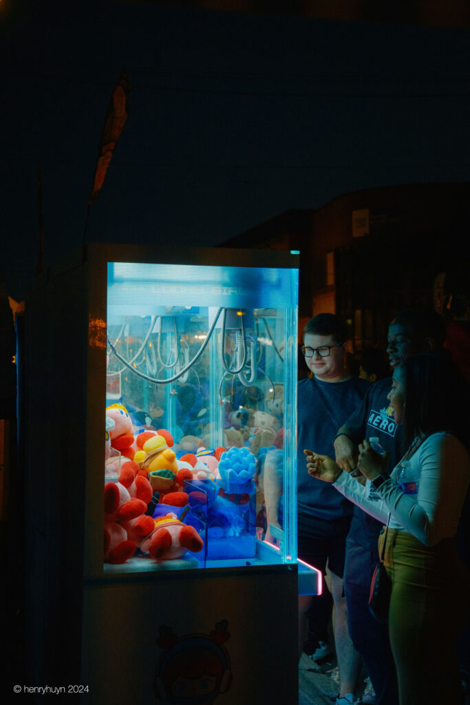 A group of friends huddles around the claw machine, excitement evident as they try their luck at capturing prizes.