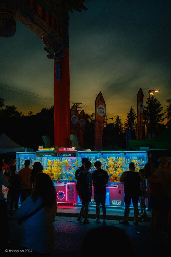 A group of people chat animatedly, bathed in the colorful glow of the claw machine in the background.